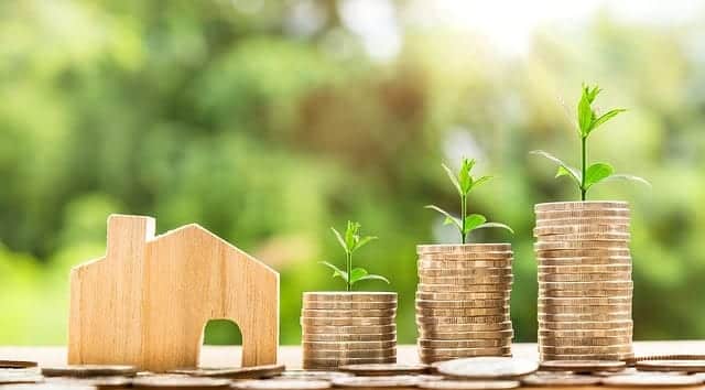 Stacks of coins with a sprout growing out of it next to a small wooded house signifying growth in semi-retirement