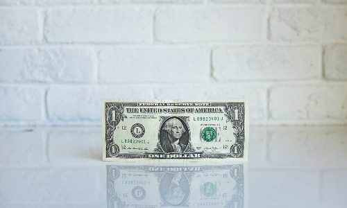 dollar bill with white brick background representing becoming a millionaire by 40
